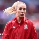 Missy Bo Kearns wearing a red jacket with an Aston Villa badge on the chest