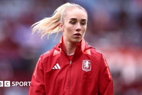 Missy Bo Kearns wearing a red jacket with an Aston Villa badge on the chest