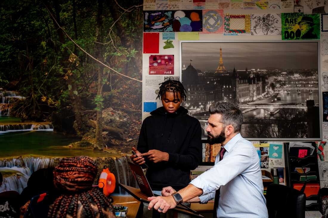 Jesse Kwakenat sits in front of a laptop computer while Walter stands next to him in a classroom at Central Senior High School in St. Paul, Minnesota, on October 9, 2025. 