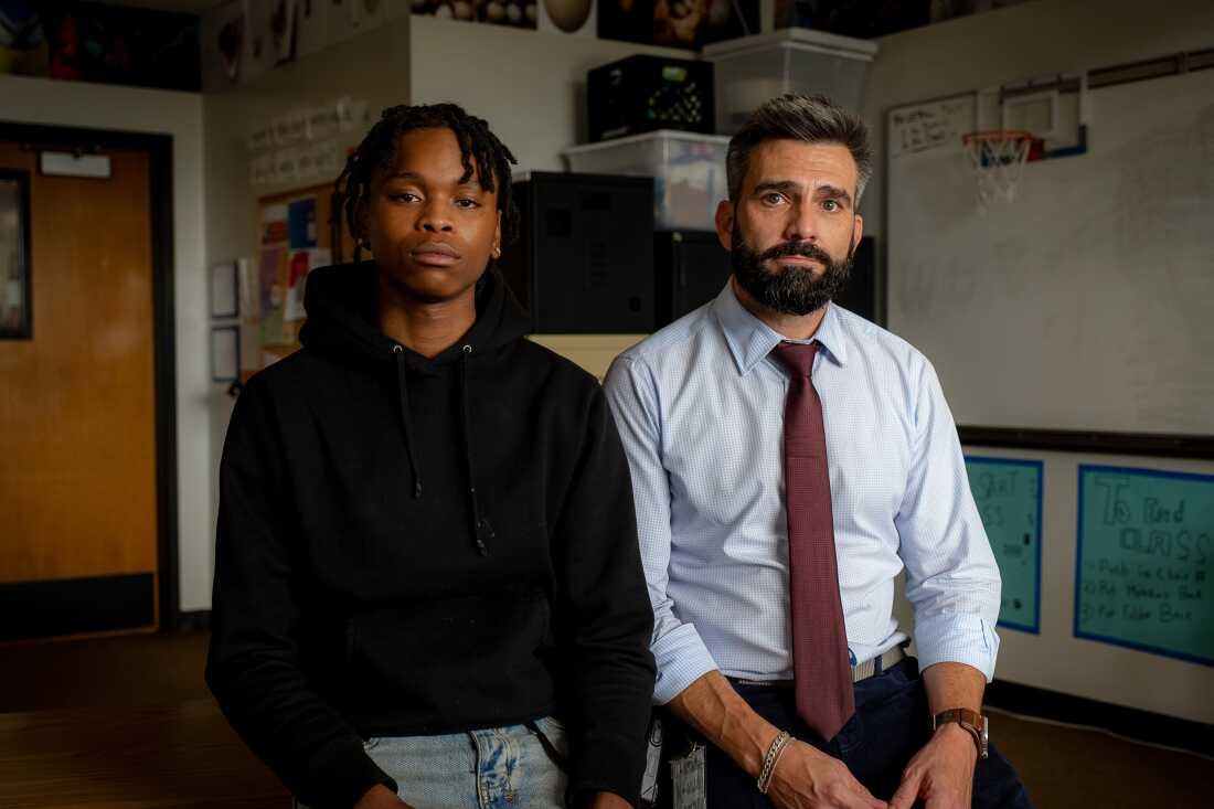 Walter sits next to Kwakenat on a desk in a classroom.