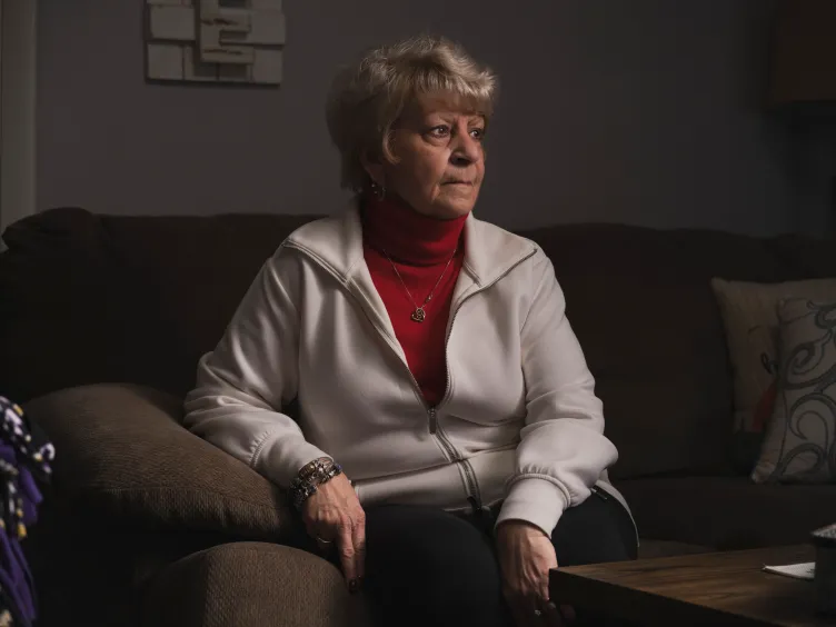A woman on a living room sofa looks off to the side with a serious expression.