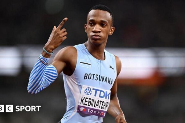 Collen Kebinatshipi shown from waist up wearing a Botswana sky blue sleeveless running jersey with his name written on a bib on the stomach, looks to his right while pointing his right index finger skywards as he prepares to compete in the men's 400m at the World Athletics Championships in Tokyo