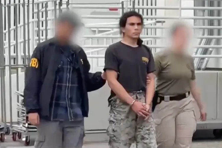 Two agents with blurred faces, one of whom has an FBI jacket on, escort a man in handcuffs.