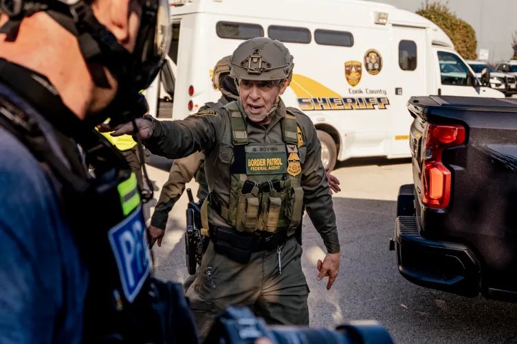 Gregory Bovino, wearing a full camouflage uniform and a helmet, points and speaks.