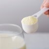A scoop of white powder is shown next to a glass of white, milky liquid. 