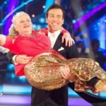 Ann Widdecombe wearing a red top and a golden glittery skirt, being held by Anton Du Beke in a tuxedo