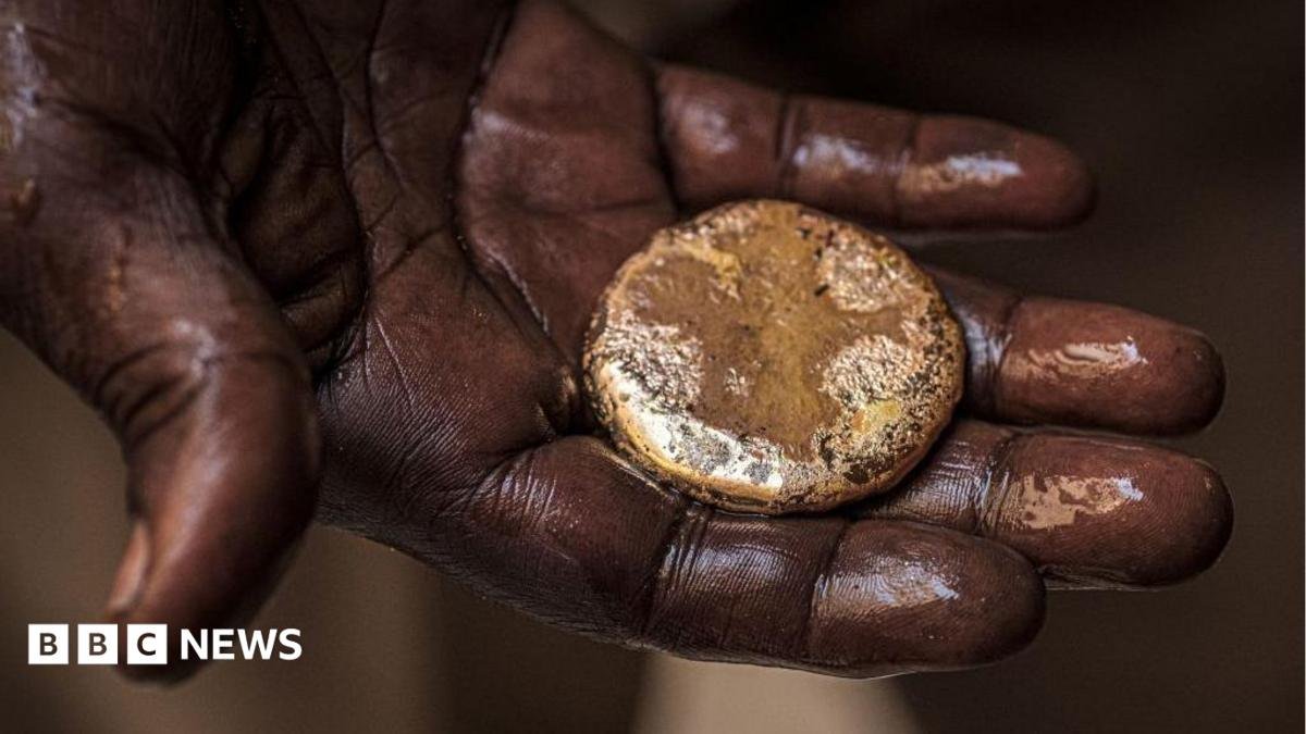 A close-up of a mud-stained hand holding a roughly circular gold nugget