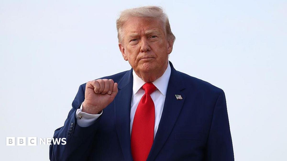 Donald Trump holds up his right fist while wearing a white shirt and red tie.
