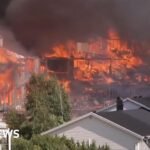 Several houses on fire engulfed in dark smoke, with untouched houses in front of them