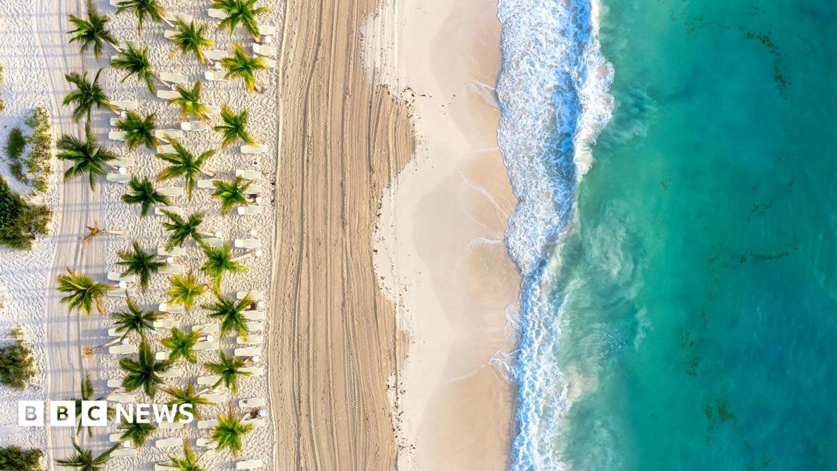 A beach in Cancun. The picture shows white sand, palm trees and an aqua sea with waves breaking on the shore