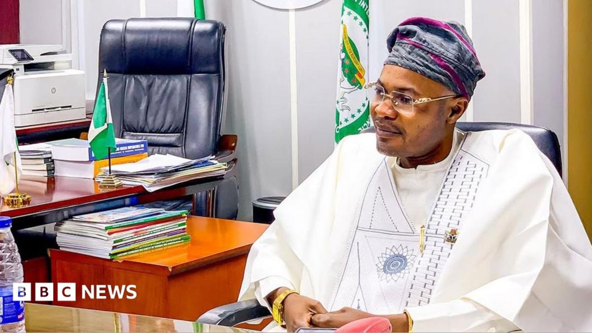 Prince Adeniyi Adeyemi Matthew, PFIPC's director general, sits in an office. He is wearing a white gown, glasses and a grey and pink cap