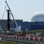 The large white dome of the Sizewell B nuclear power plant is the backdrop of the picture which has construction work and cranes in the foreground. The white dome sits on large square grey coloured buildings.