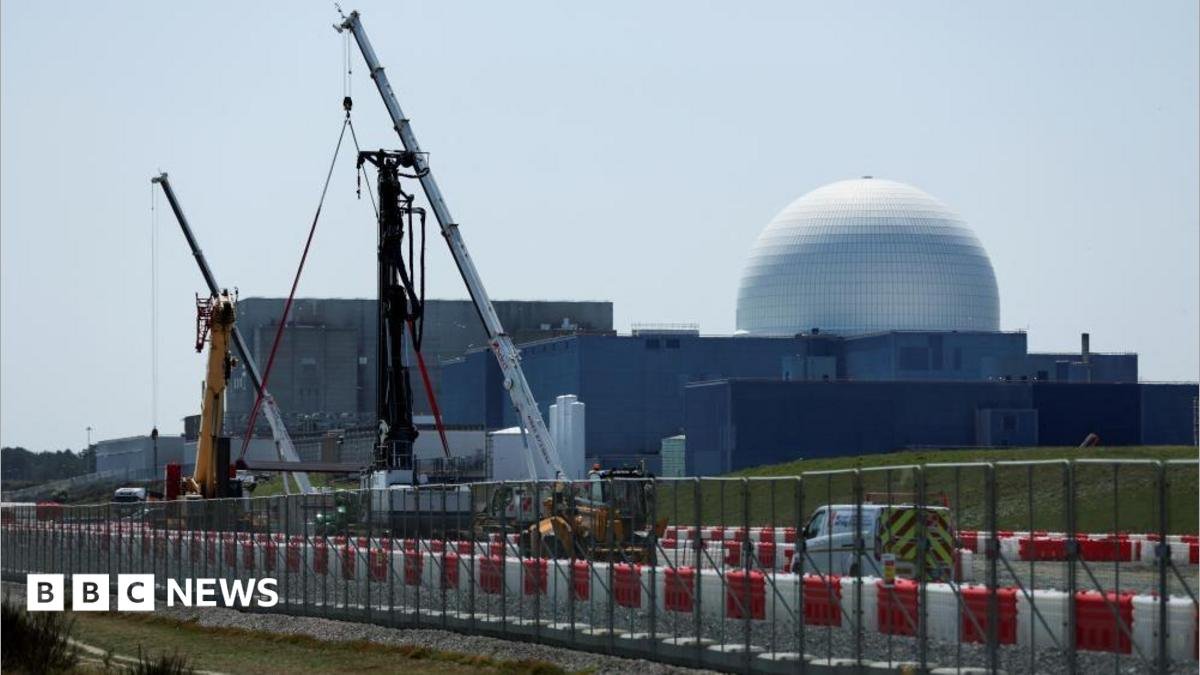 The large white dome of the Sizewell B nuclear power plant is the backdrop of the picture which has construction work and cranes in the foreground. The white dome sits on large square grey coloured buildings.