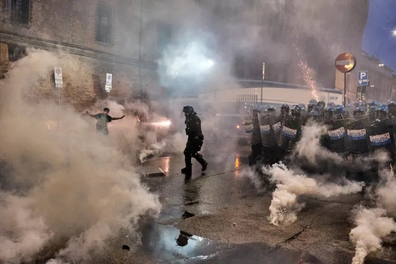 A protester moves through smoke as police stand nearby during clashes in Bologna following demonstrations over Abderrahim Fakir’s death.