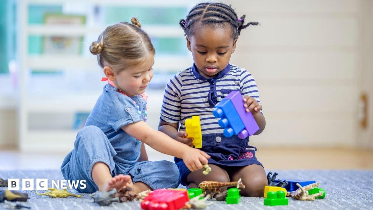 Stock image of two toddlers - one girl and one boy - playing with toy bricks on a carpet