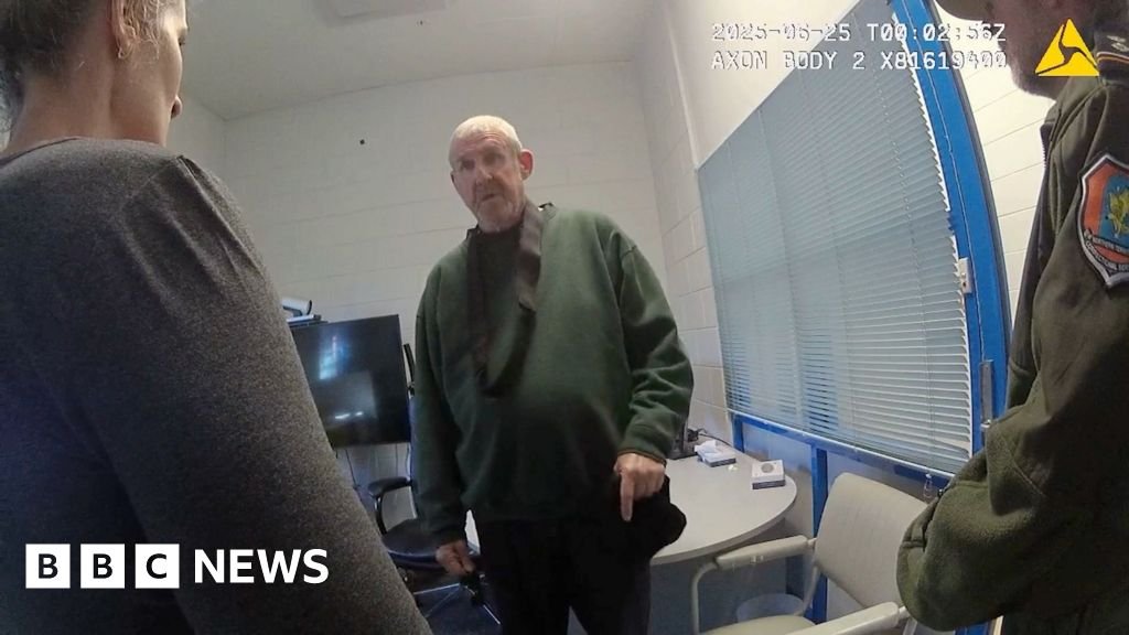 Murdoch wearing dark green jumper stands in front of camera while questioned by two officers in front of him