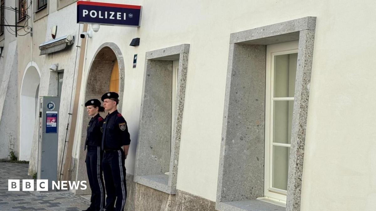 Two police officers stand outside a white-washed building with a police sign in German on the wall