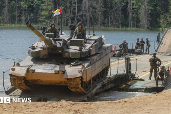 Polish and Lithuanian armed forces in camouflage combat gear are seen conducting tactial water-crossing operations with a tank at a lake in Poland