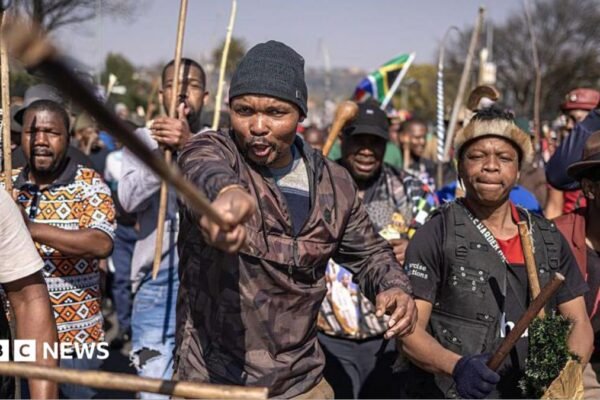 Protesters marching, a man at the front is pointing a stick at the camera.