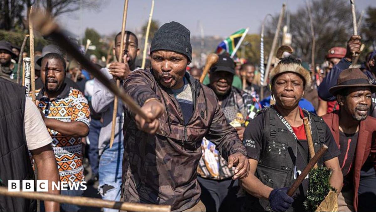 Protesters marching, a man at the front is pointing a stick at the camera.