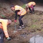 Volunteers in high viz on the floor of a river with almost no water lifting soil and silt